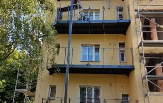 Instalace ocelových balkonů s zábradlím Instalace nových ocelových balkonů se skleněným zábradlím na fasádu bytového domu. Realizace KOVKOM.