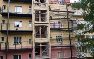Montáž nových balkonů se zábradlím Nově instalované balkony se skleněným zábradlím na fasádě bytového domu, vpravo probíhá rekonstrukce.