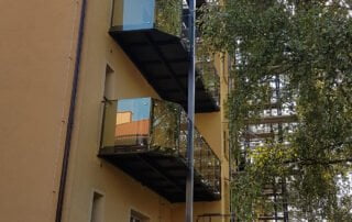 Ocelové balkony se skleněným zábradlím Moderní ocelové balkony s proskleným zábradlím na žluté fasádě domu, detailní pohled zespodu.