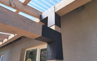 Kovové spojky pro dřevěnou pergolu Detail pergoly s dřevěnými trámy a černými kovovými spojovacími prvky. Průhledná střešní krytina.