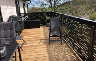 Zakázkové kovové zábradlí terasa Kovové zábradlí s moderním laserem řezaným vzorem na dřevěné terase. Realizace zakázkové kovovýroby KOVKOM.