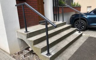 Kovové zábradlí venkovní schody instalace Nové černé kovové zábradlí na venkovních betonových schodech u vstupu do domu, realizace KOVKOM.