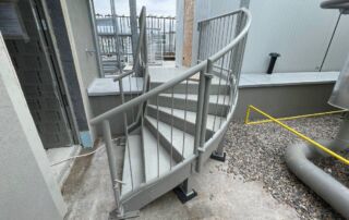 Kovové spirálové schodiště KOVKOM s protiskluzovými nášlapy a ocelovým zábradlím, instalované na průmyslové budově.