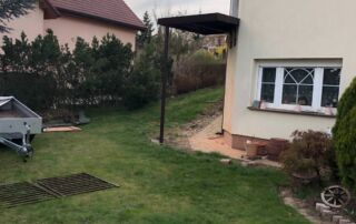 Kovový přístřešek u domu realizace Tmavý kovový přístřešek s jedním sloupem instalovaný u rodinného domu. Zakázková výroba KOVKOM.