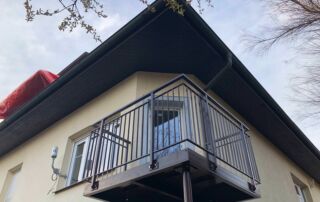 Nový kovový balkon s montáží Nový kovový balkon s tmavým zábradlím a konstrukcí, instalovaný na fasádě domu. Realizace zakázkové kovovýroby KOVKOM.