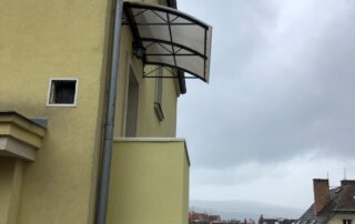 Kovový přístřešek nad vchodem Nový kovový přístřešek s polykarbonátovou deskou nad vchodem žlutého domu, zakázková výroba KOVKOM.