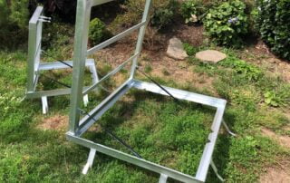 Ocelové rámy s plynovými vzpěrami Dva zakázkové galvanizované ocelové rámy s plynovými vzpěrami na trávě, připravené k instalaci brány nebo poklopu.