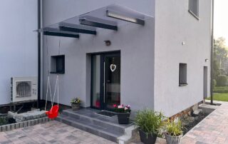 Moderní skleněný přístřešek KOVKOM Moderní skleněný přístřešek nad vchodovými dveřmi rodinného domu, instalace KOVKOM.
