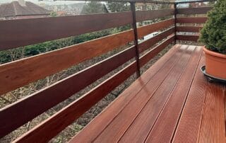 Nový balkon s dřevěnou terasou a kovovým zábradlím s dřevěnou výplní, výhled na město.