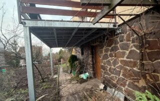 Zakázková ocelová konstrukce terasy s dřevěnou pergolou u kamenného domu. Realizace kovovýroby KOVKOM.