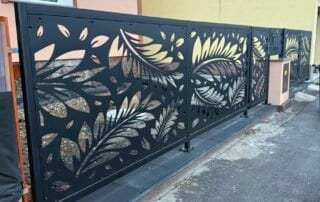 Moderní kovový plot s laserem řezaným dekorem listů u vily, v pozadí viditelný balkon KOVKOM.