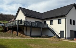 Terasy a přístřešky 20 Celkový pohled na dům s hotovou ocelovou terasou a zábradlím i schody na terasu.