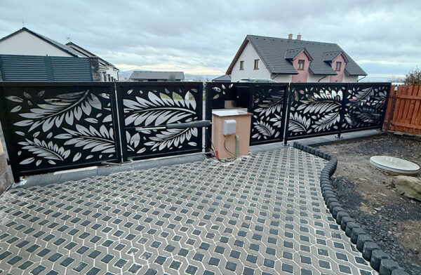 Zakázková posuvná brána s laserem řezaným listovým vzorem a automatickým pohonem. Realizace KOVKOM u rodinného domu.