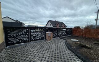 Designový kovový plot s listovým vzorem, brankou a samonosnou skládanou bránou s pohonem, dlážděná příjezdová cesta.