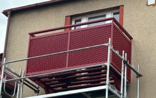 Nový červený kovový balkon s mřížkovou výplní během montáže. Zakázková výroba a instalace balkonů KOVKOM.