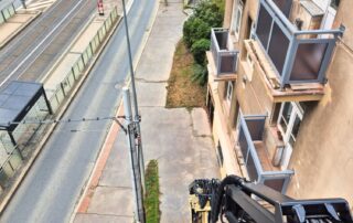 Nové balkonové zábradlí na bytovém domě, pohled shora během montáže s využitím pracovní plošiny.