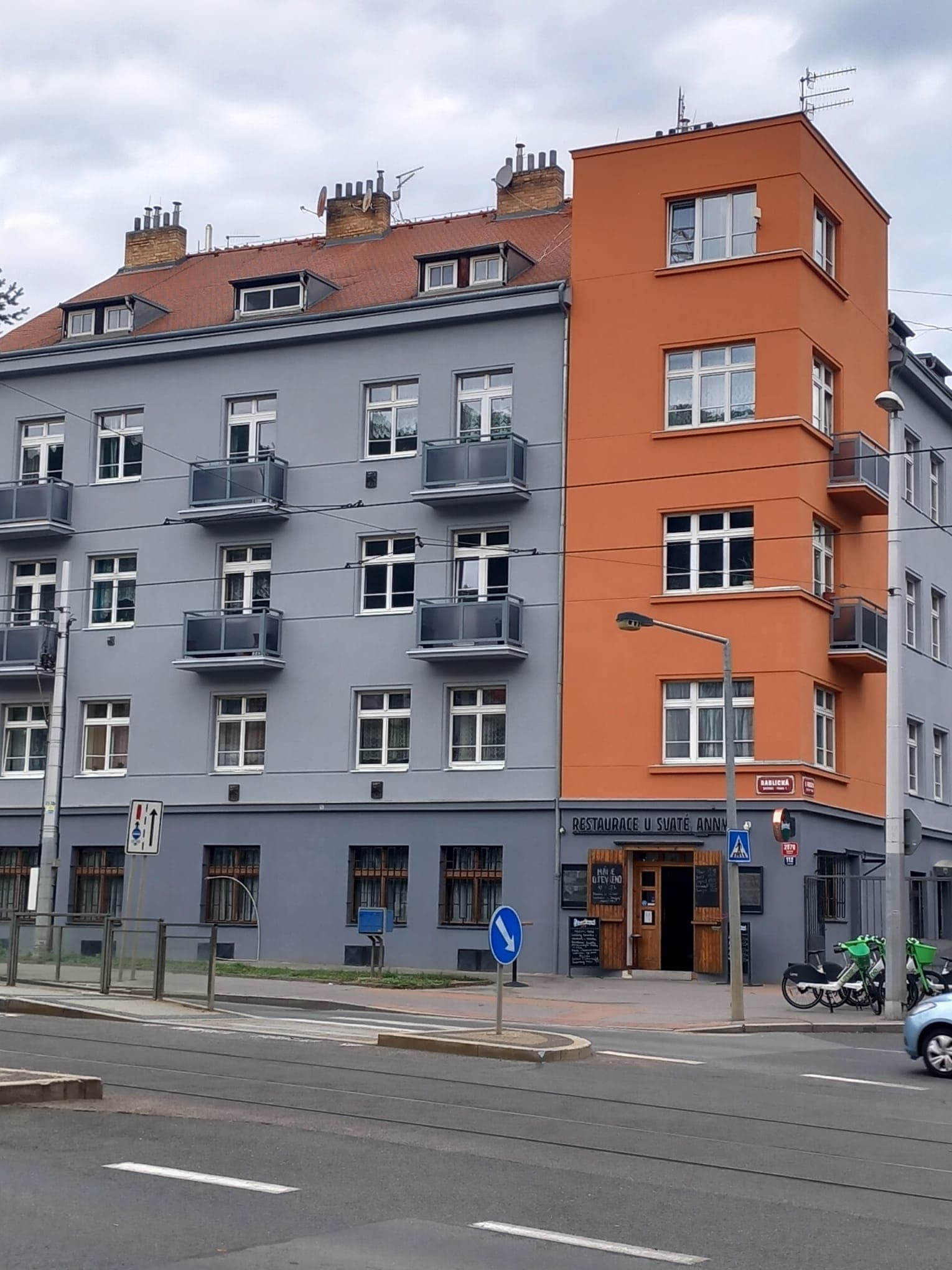 Nové balkonové zábradlí z oceli v antracitové barvě na bytovém domě s oranžovou fasádou.