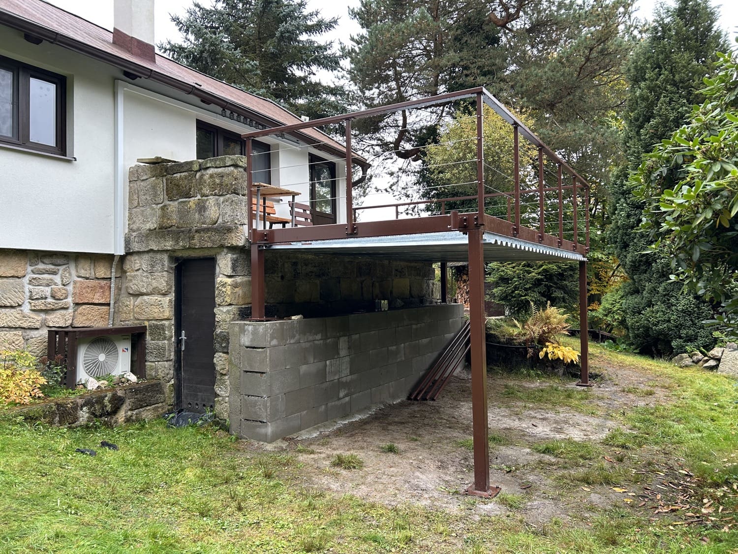 Rozšíření terasy na podpěrných sloupech s kovovým zábradlím, realizace pro chalupu v CHKO.