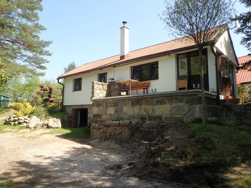 Rozšíření terasy na podpěrných sloupech pro chalupu s kamenným soklem a dřevěným posezením.